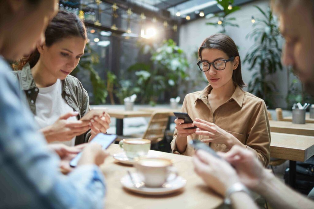 Group of young people sitting at table in cafe and using smartphones in silence, copy space
